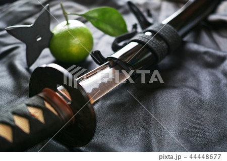 黒い布の上の抜きかけた日本刀と手裏剣が刺さったミカン 44448677