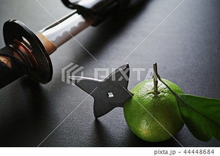 黒い板の上の抜きかけた日本刀と手裏剣が刺さったミカン 44448684