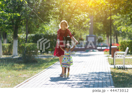 Mom and daughter are walking along the sidewalk. 44473012