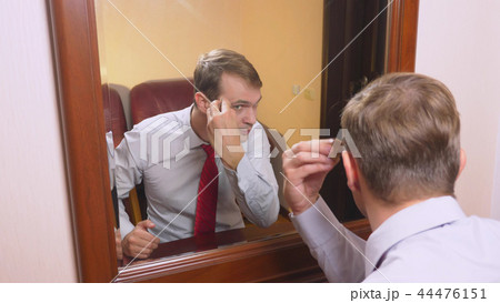 the concept of metrosexualism. a handsome man in front of a mirror takes care of his face. does the 44476151