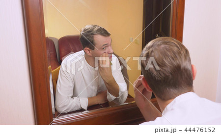 the concept of metrosexualism. a handsome man in front of a mirror takes care of his face. does the 44476152
