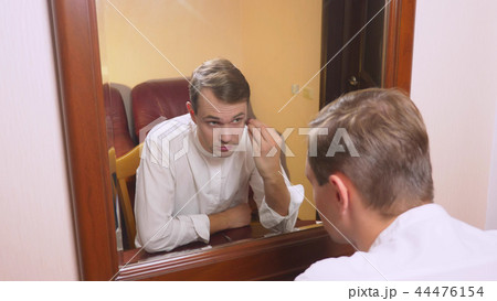 the concept of metrosexualism. a handsome man in front of a mirror takes care of his face. does the 44476154