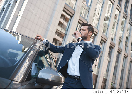 Confident businessman drinking coffee to go while standing near car on street 44487513