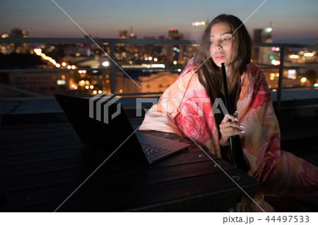Girl sits wrapped in a blanket and smokes a hookah. Girl sits wrapped in a blanket and smokes a hookah. 44497533