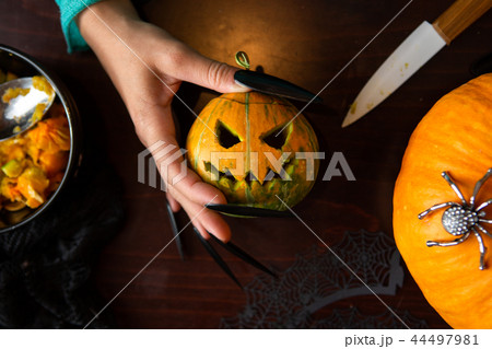 Photo of man's hands with pumpkin jack, knife sitting at wooden table 44497981
