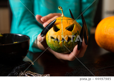 Image of hands holding jack-o-lantern from pumpkin sitting at wooden table Image of hands holding jack-o-lantern from pumpkin sitting at wooden table 44497985