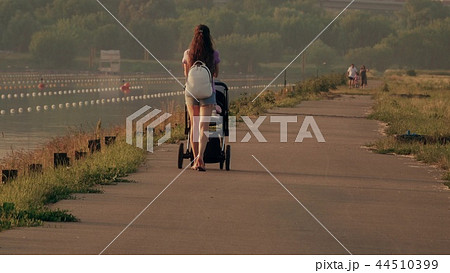 Beautiful young woman pushing stroller along waterfront pathway Beautiful young woman pushing stroller along waterfront pathway 44510399