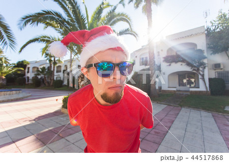 Joke, holidays and christmas concept - young funny cheerful man in santa hat holding sunglasses 44517868