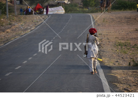 インドのプシュカル　砂漠の道路を歩く楽器奏者のインド人男性　ターバンと民族衣装と手造り楽器を持参 44523421