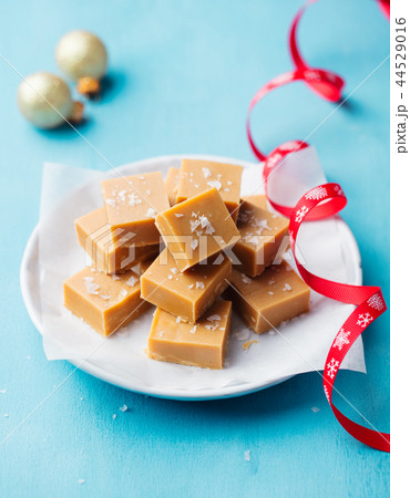 Fresh caramel fudge candies on a plate with Christmas red ribbon on blue background. Fresh caramel fudge candies on a plate with Christmas red ribbon on blue background. 44529016