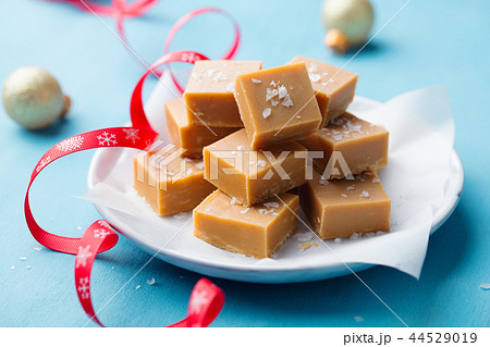 Fresh caramel fudge candies on a plate with Christmas red ribbon on blue background. Close up. 44529019