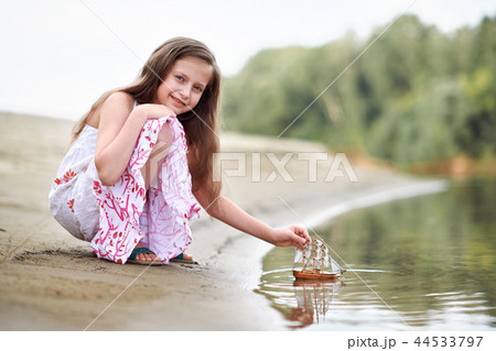 girl child playing with toy sailing ship by river 44533797