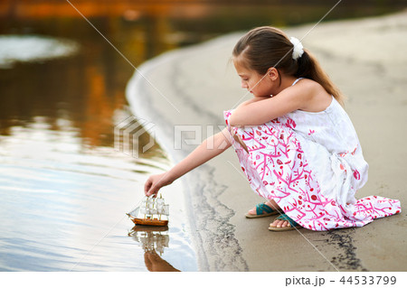 girl child playing with toy sailing ship by river 44533799