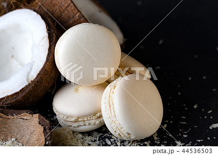 Coconut halves with white macaroons on dark background minimal creative concept. Coconut halves with white macaroons on dark background minimal creative concept. 44536503