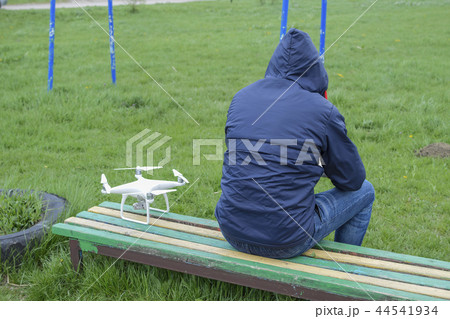 A man with a remote control quadroopter in his hands is sitting on a bench. White quadroopter A man with a remote control quadroopter in his hands is sitting on a bench. White quadroopter 44541934