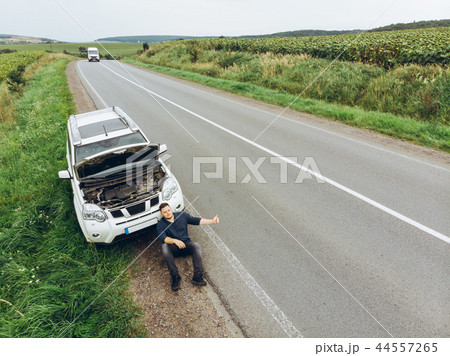 man sitting on road near broken car. trying stop car for help 44557265