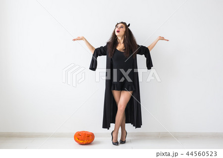 Portrait of a stylish brunette woman with halloween pumpkin over light background with copy space 44560523