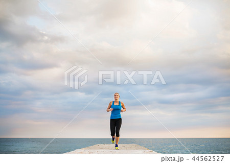 A young sporty woman running on a pier by the ocean outside. A young sporty woman running on a pier by the ocean outside. 44562527