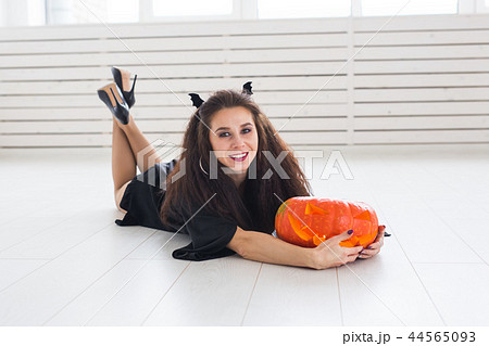 Smiling brunette woman in halloween makeup posing with carved pumpkin 44565093