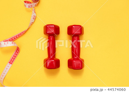 Two red dumbbells and tape measure. Fitness concept Two red dumbbells and tape measure. Fitness concept 44574060