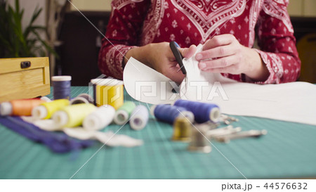 Middle-age woman hands with scissors cutting paper template. Handmade cloth. 44576632