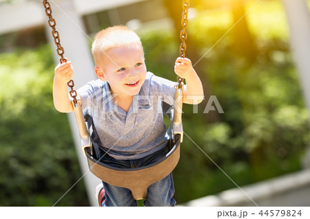 Happy Young Boy Having Fun On The Swings At The Playground Happy Young Boy Having Fun On The Swings At The Playground 44579824