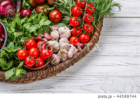 On a white wooden background, a basket of fresh vegetables. 44589744