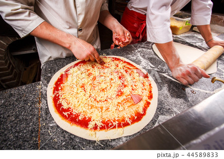 Adding cheese to pizza. Dough on the table. 44589833