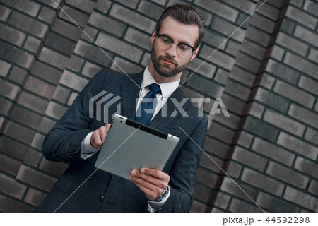 A young businessman in glasses and an expensive suit, works on a tablet in his hands 44592298