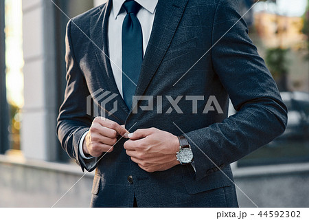 A young businessman fastens a suit jacket. He has on his hands an expensive watch. 44592302