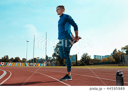 Man runner stretching legs preparing for run training on stadium tracks doing warm-up Man runner stretching legs preparing for run training on stadium tracks doing warm-up 44595989