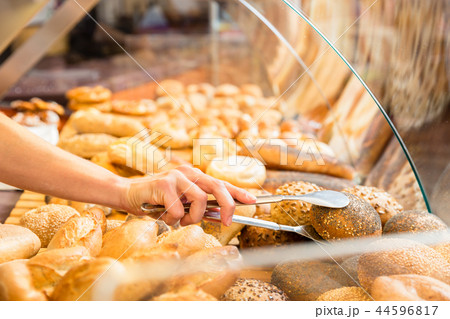 Sales woman in baker shop putting bread roll in paper bag 44596817