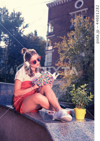Bright stylish girl listening to music in earphones and reading interesting book Bright stylish girl listening to music in earphones and reading interesting book 44601282