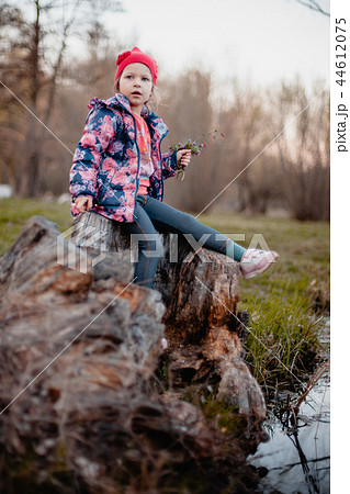A little girl is sitting on a stump near a stream. A little girl is sitting on a stump near a stream. 44612075