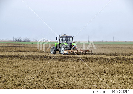 Lush and loosen the soil on the field before sowing. The tractor plows a field with a plow Lush and loosen the soil on the field before sowing. The tractor plows a field with a plow 44630894