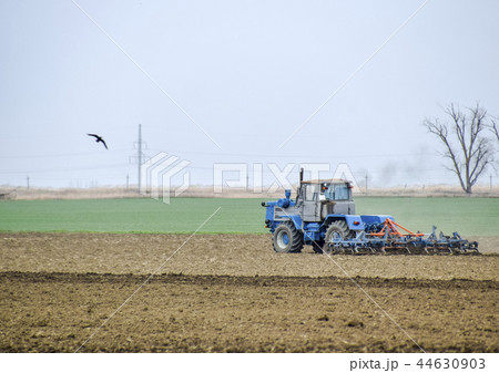 Lush and loosen the soil on the field before sowing. The tractor plows a field with a plow Lush and loosen the soil on the field before sowing. The tractor plows a field with a plow 44630903