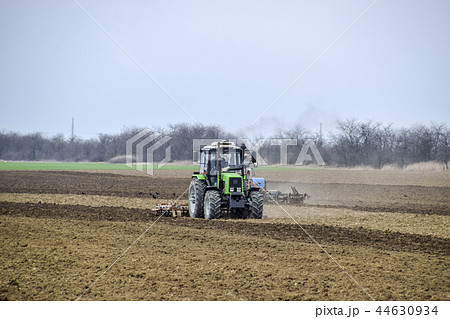 Lush and loosen the soil on the field before sowing. The tractor plows a field with a plow Lush and loosen the soil on the field before sowing. The tractor plows a field with a plow 44630934