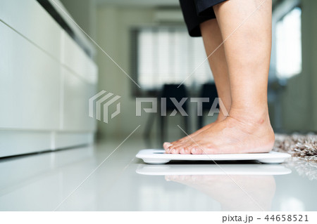 old woman standing on weight scale in living room 44658521