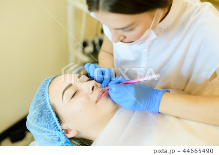 Skilled female cosmetologist shaping lips with pencil for young girl before microblading. Skilled female cosmetologist shaping lips with pencil for young girl before microblading. 44665490