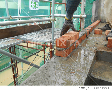 Workers laying brick to form brick wall 44671993