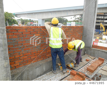 Workers laying brick to form brick wall 44671995