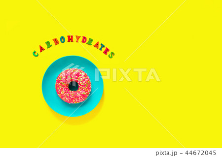 Carbohydrates and pink donut on plate on yellow  44672045
