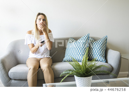 Women watching TV on the sofa at home with remote control Women watching TV on the sofa at home with remote control 44676258