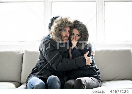 Couple have cold on the sofa at home with winter coat Couple have cold on the sofa at home with winter coat 44677126