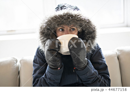 Woman have cold drink coffee on the sofa at home with winter coat Woman have cold drink coffee on the sofa at home with winter coat 44677158