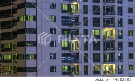 Windows of the multi-storey building of glass and steel lighting inside and moving people within timelapse 44682603