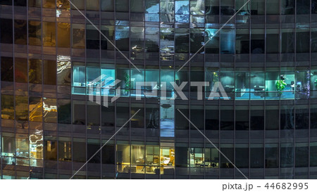 Windows of the multi-storey building of glass and steel lighting inside and moving people within timelapse 44682995
