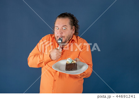 Funny fat man in orange shirt with a piece of chocolate cake on a plate 44691241