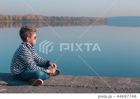 Child sitting at waterfront in warm autumn light Child sitting at waterfront in warm autumn light 44697746