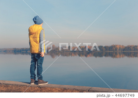 Child standing at waterfront in warm autumn light Child standing at waterfront in warm autumn light 44697749